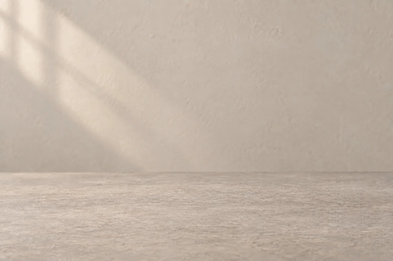 Empty warm-gray tabletop and beige wall lit softly from the upper left